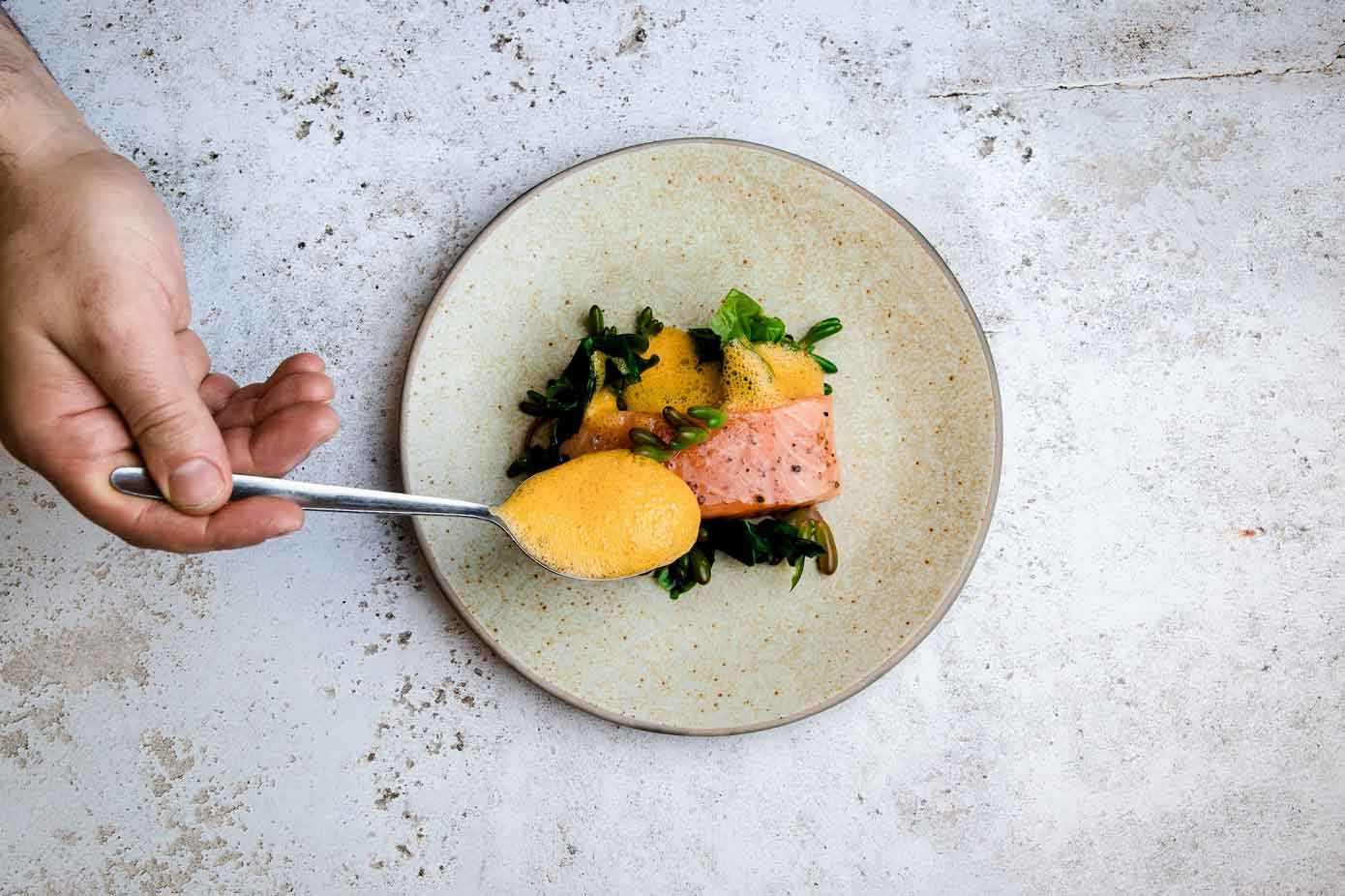 Chef pouring sauce over a salmon fillet.