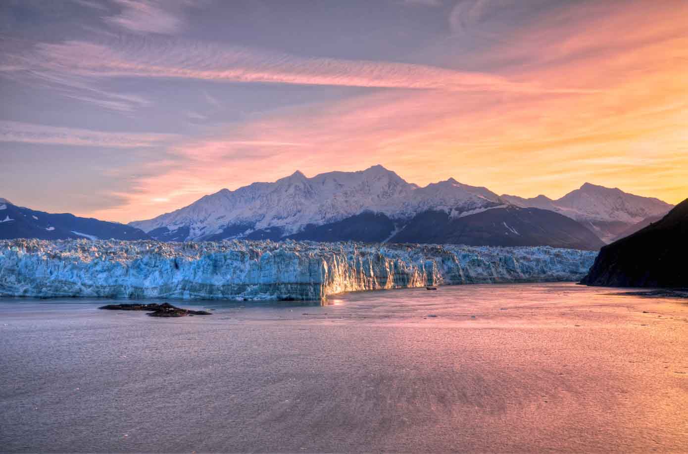 Sunrise as seen from the ocean peaking over a glacier in Alaska.