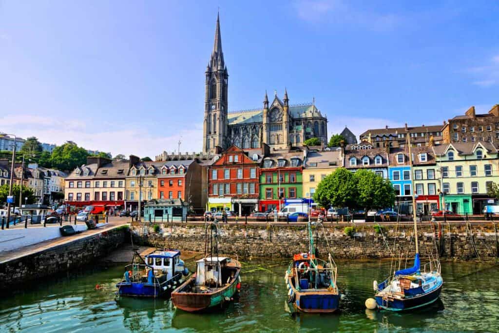 Colorful buildings and old boats with cathedral in background in the harbor of Cobh, County Cork, Ireland.