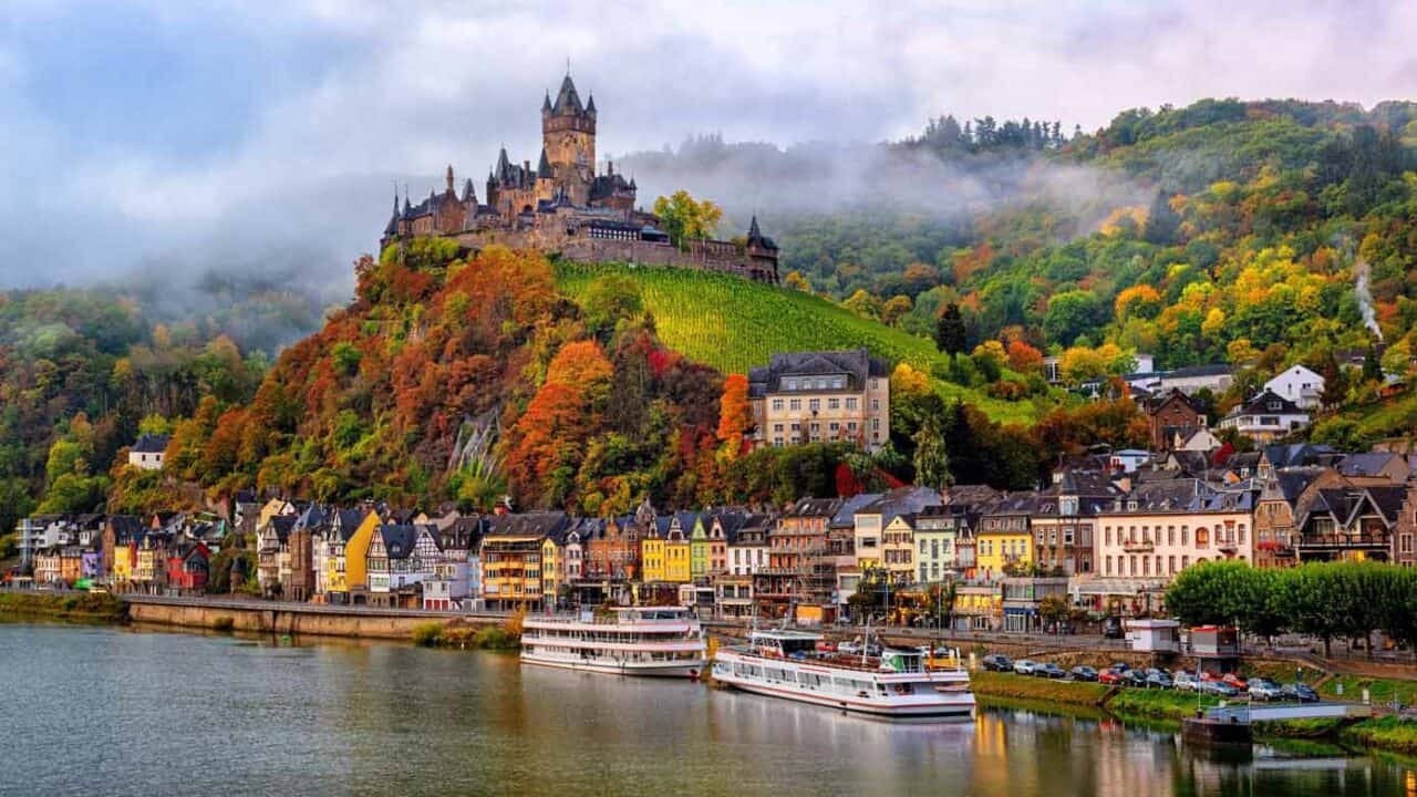 Reichsburg Castle on a hill along a river on a cloud day during autumn.