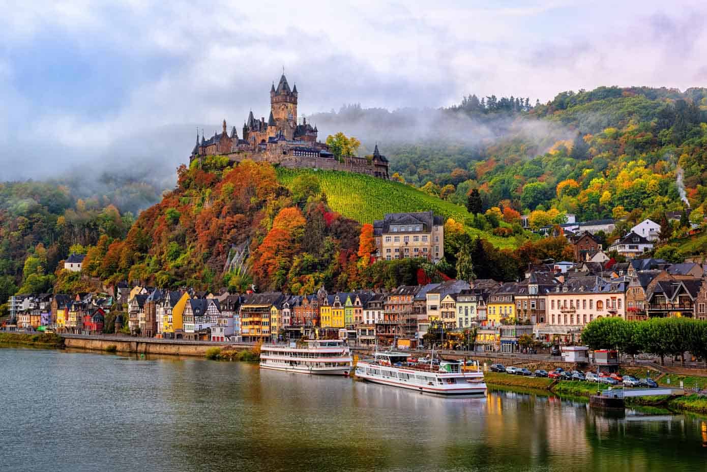 Reichsburg Castle on a hill along a river on a cloud day during autumn.