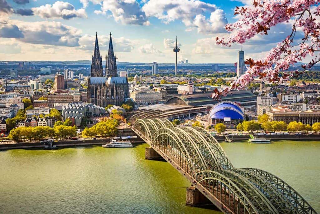 Bridge crossing river with church and city skyline in background during springtime.