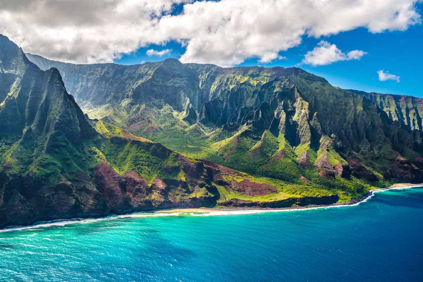 Majestic sea cliffs on the Napali Coast of Hawaii sloping into a bright blue ocean.