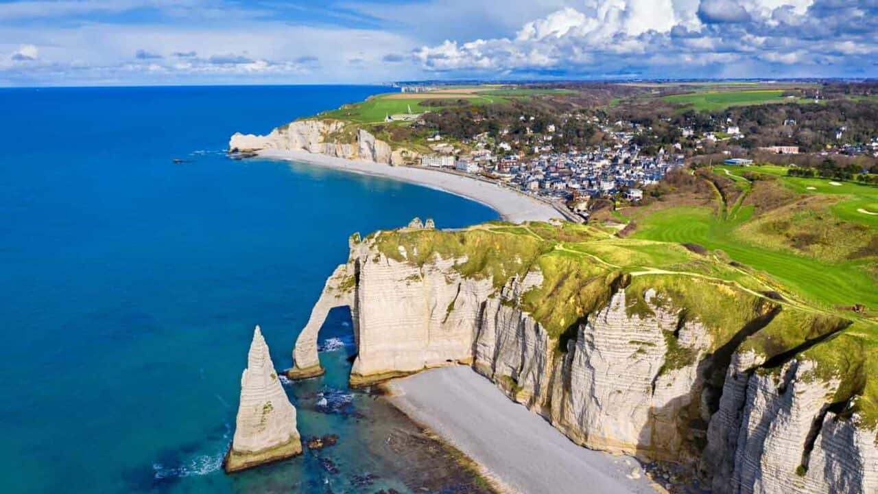 Huge cliffs, blue ocean, and spanning beaches with a little village in Normandy, France.