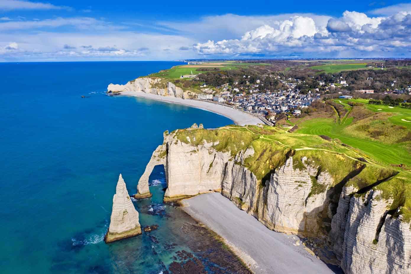 Huge cliffs, blue ocean, and spanning beaches with a little village in Normandy, France.