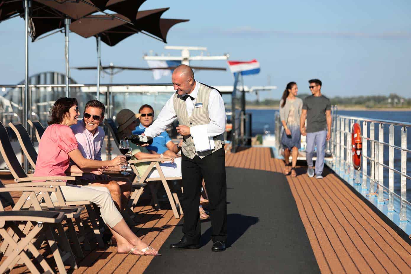 Waiter pouring a glass of wine for a couple on a river cruise ship on a sunny day.