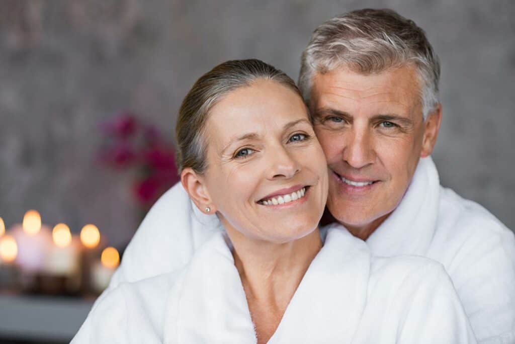 Happy senior older couple inside cruise ship spa with bathrobes on.