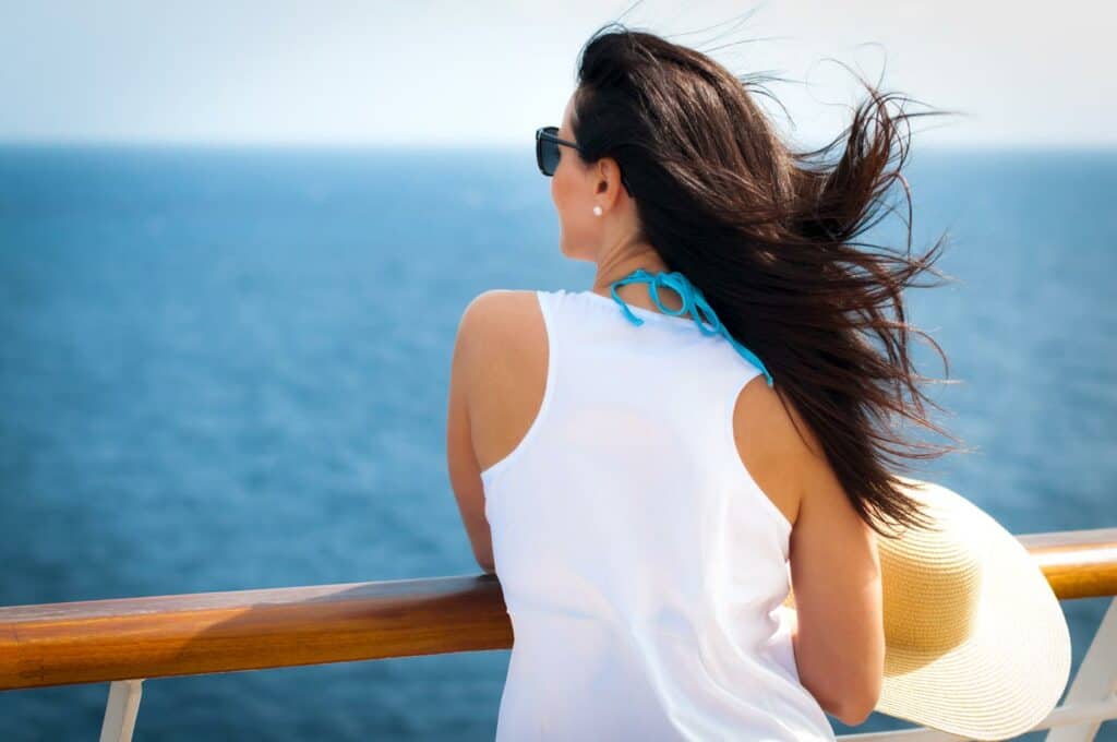 A single woman standing on the cruise ship deck balcony with an ocean view and wind in her hair.